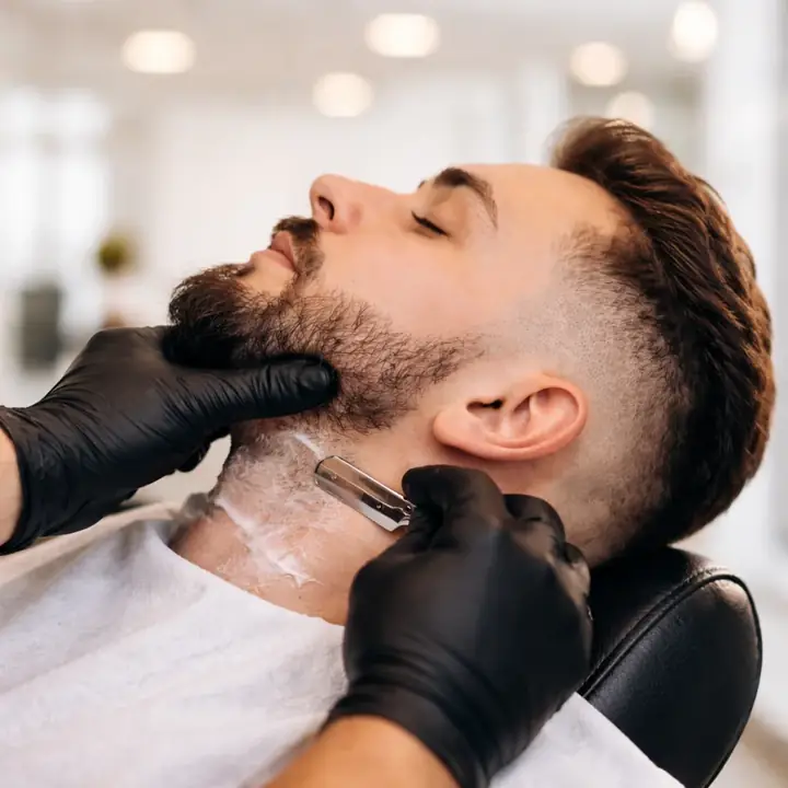 Barba sendo aparada com navalha e luvas pretas
